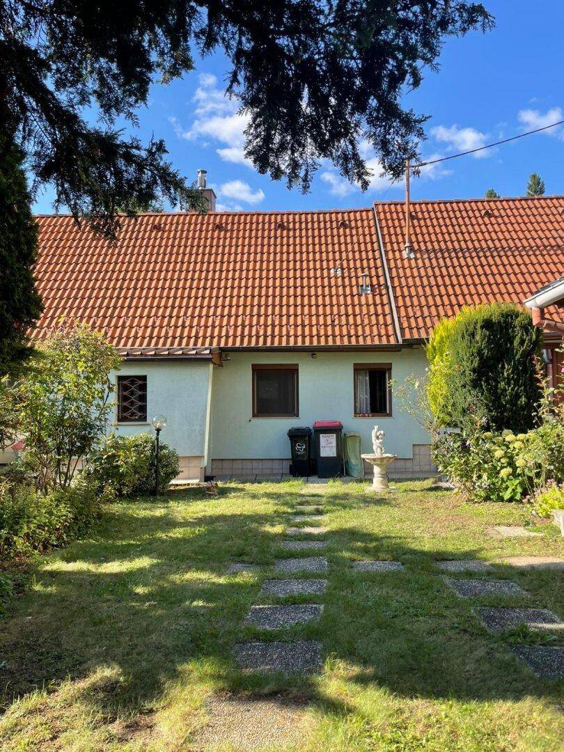 Rückansicht des Hauses mit Garten, Rasenfläche und dekorativer Gartenstatue unter blauem Himmel.