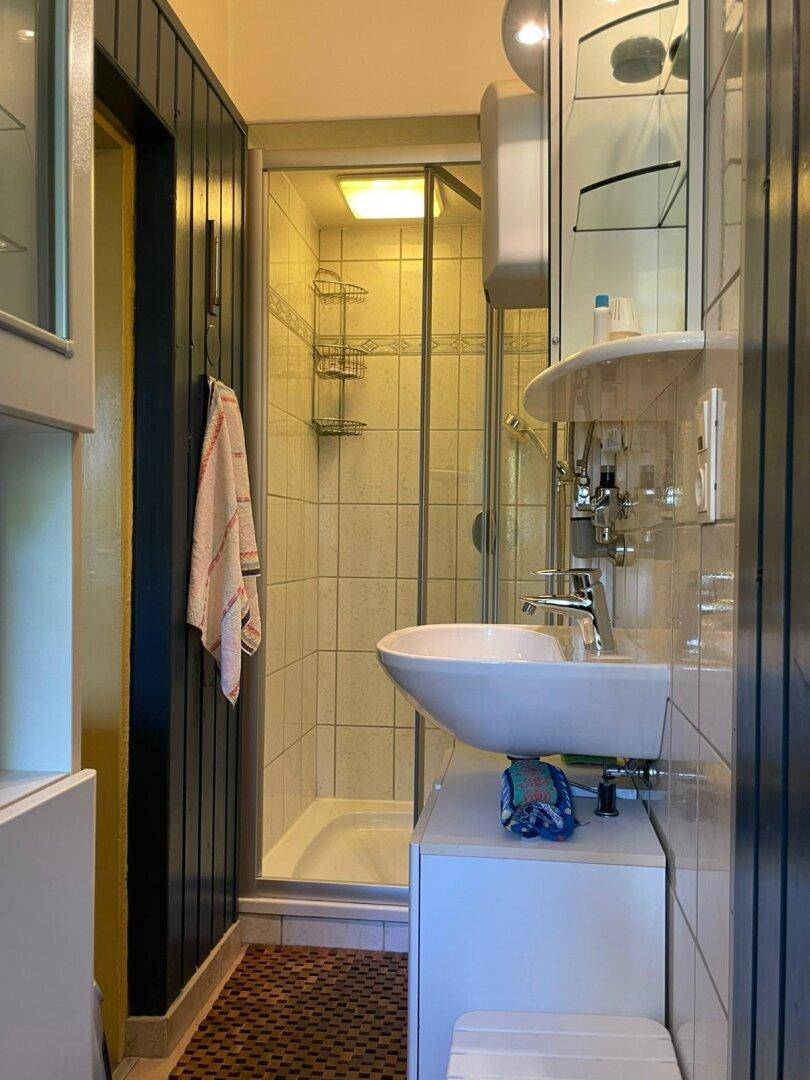 Kleines Badezimmer mit Duschkabine, Waschbecken und hellen Fliesen an den Wänden.