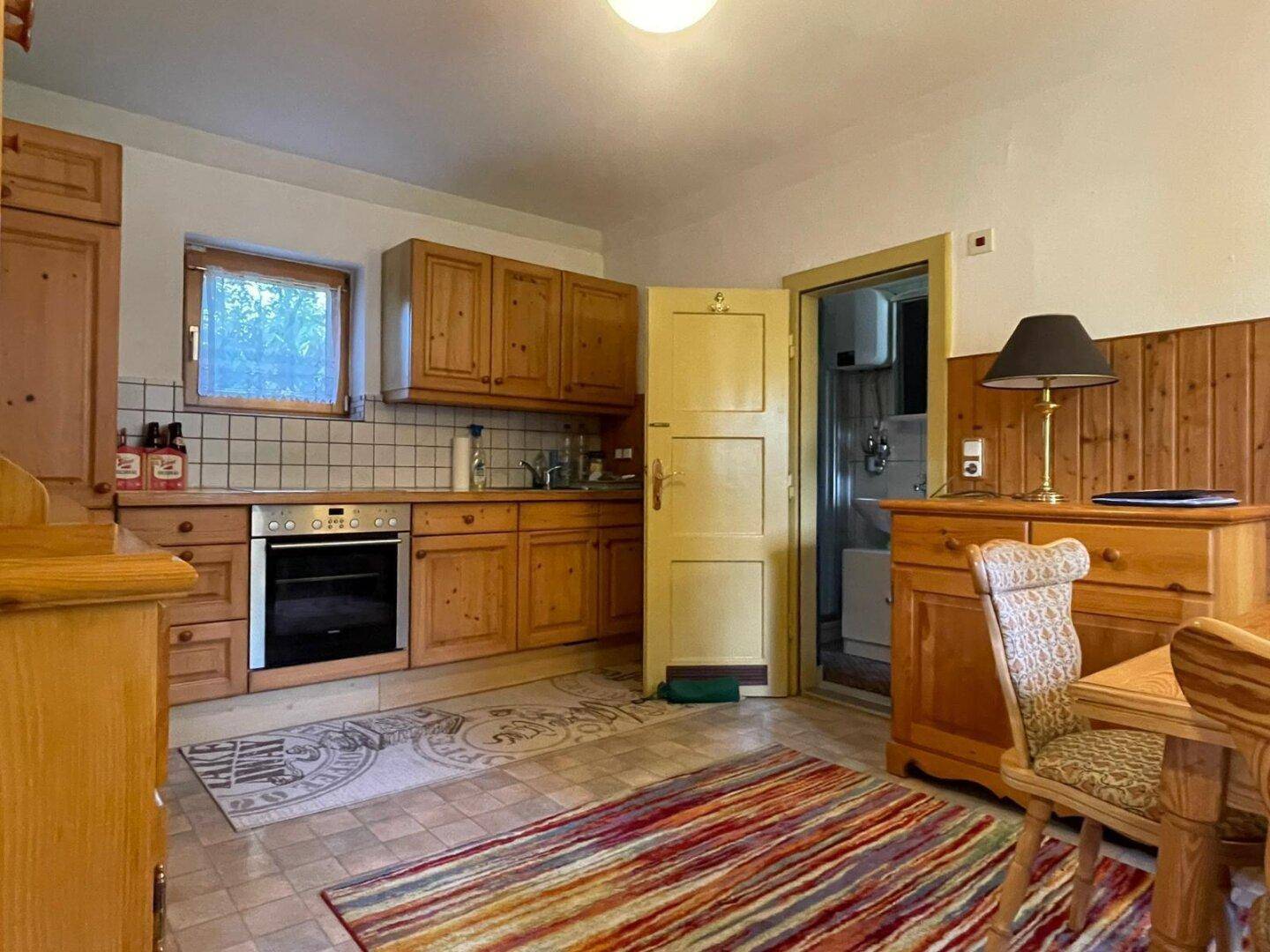 Gemütliche Küche im Landhausstil mit Holzschränken, Fliesenboden und Blick ins Badezimmer.