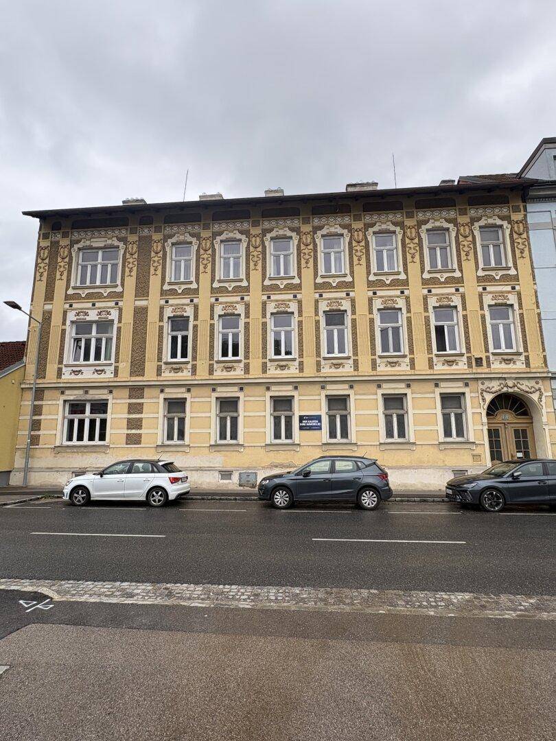 Historisches Mehrfamilienhaus mit reich verzierter Fassade und Parkplätzen an der Straße.
