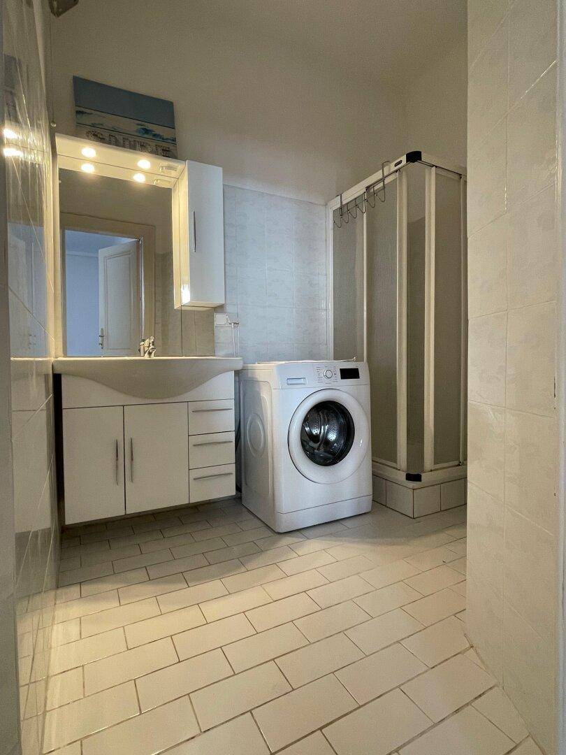 Funktionales Badezimmer mit Dusche, Waschbecken, Waschmaschine und hellen Fliesen.
