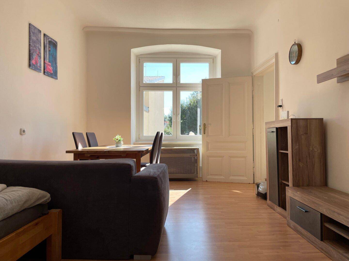 Gemütlicher Wohn-Essbereich mit Holzboden, großem Fenster und einfacher Einrichtung.
