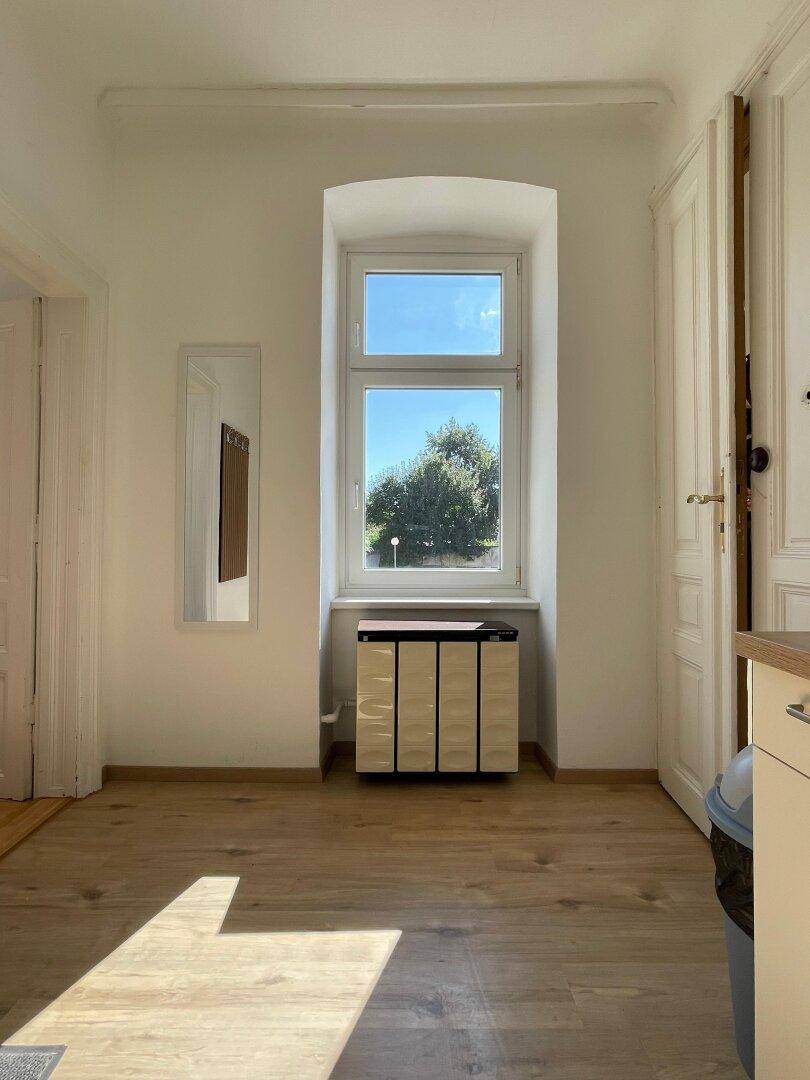 Heller Flur mit Holzboden und einem Fenster, das Tageslicht hereinlässt.