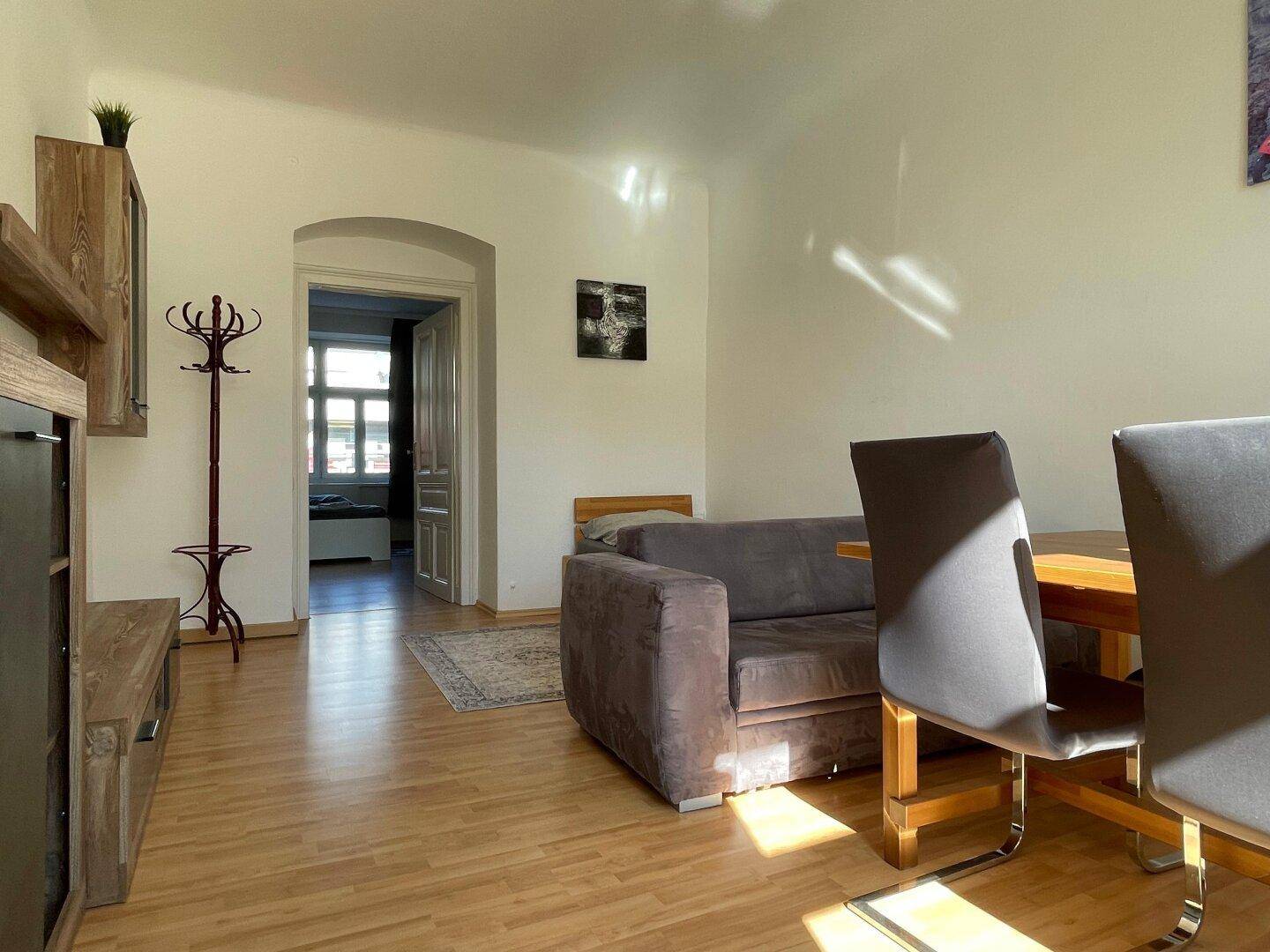 Heller Wohnbereich mit Holzboden, Sofa und Blick in einen weiteren Raum.