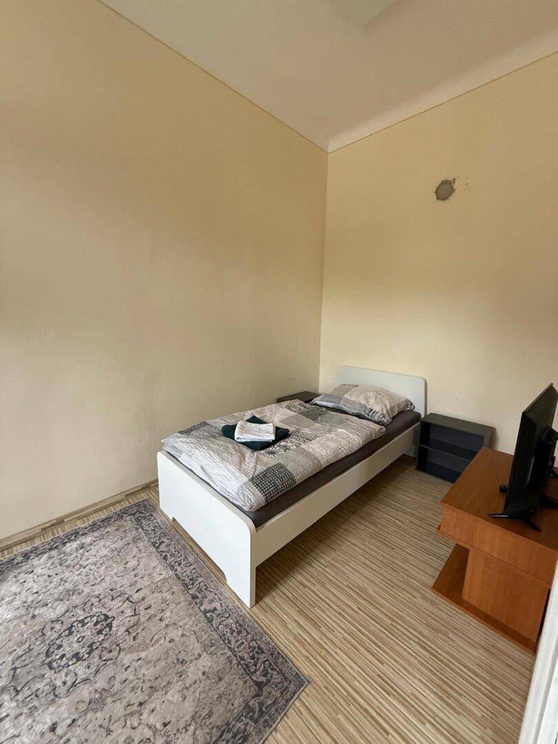 Einfaches Schlafzimmer mit Einzelbett, Holzboden und Fernseher.