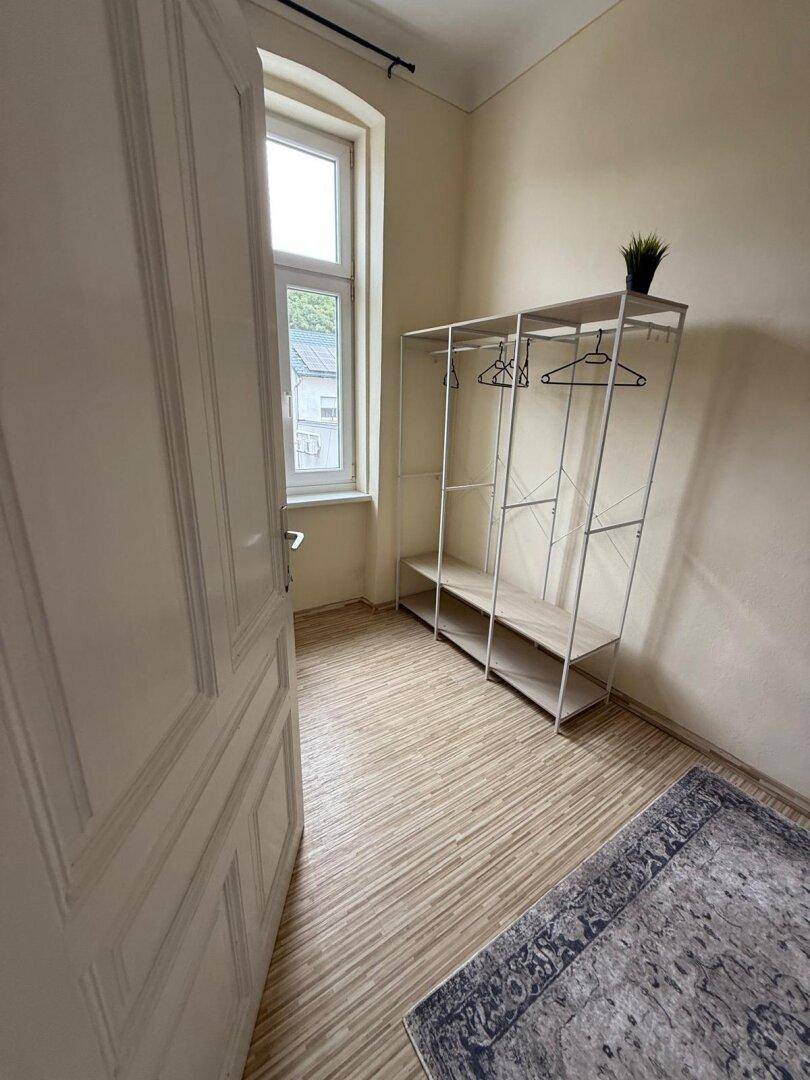 Heller Raum mit Holzboden, Fenster und einem offenen Kleiderständer.