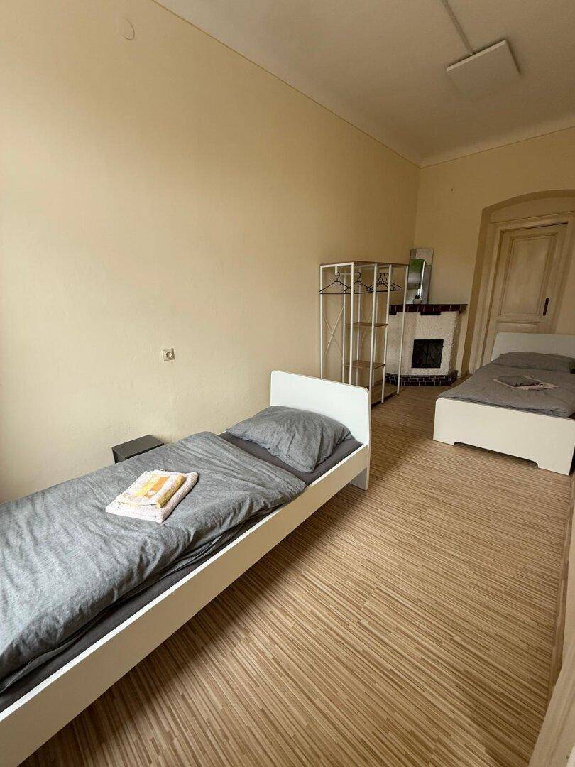 Geräumiges Schlafzimmer mit zwei Betten, Holzboden und einem Kachelofen.