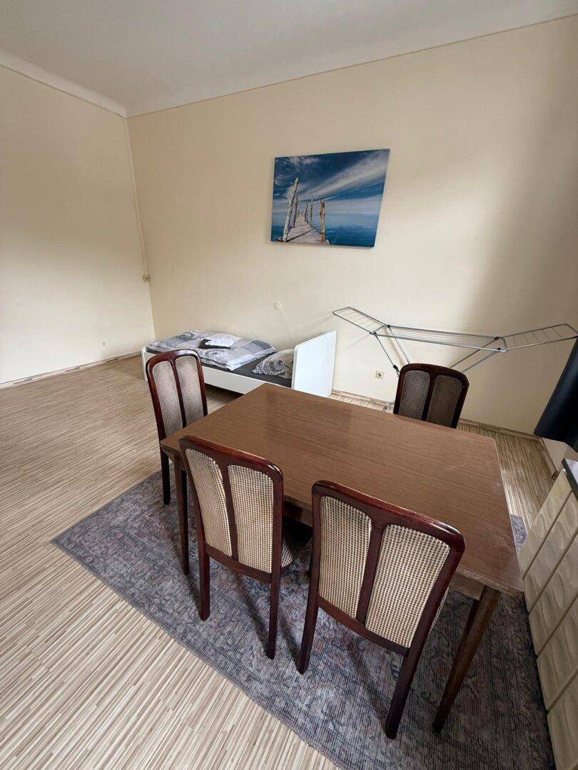 Kombinierter Wohn- und Essbereich mit Holzboden, Esstisch und Bett.