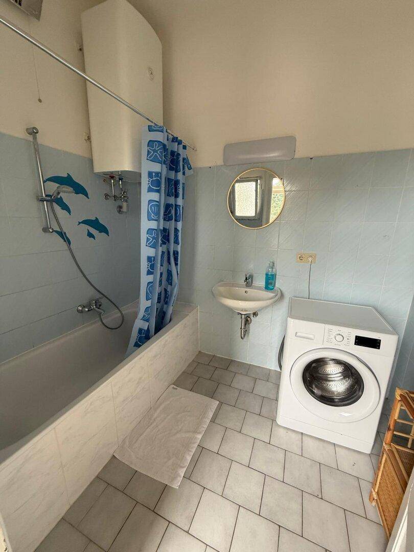 Badezimmer mit Badewanne, Waschbecken, Waschmaschine und blauen Fliesen.
