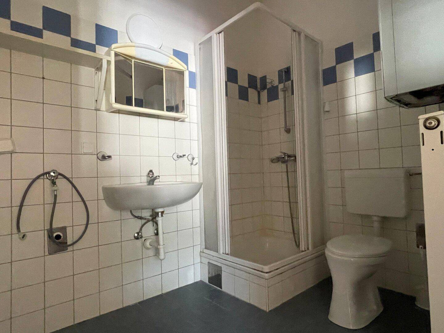 Altes Badezimmer mit Dusche, WC, Waschbecken und blauen Fliesen.
