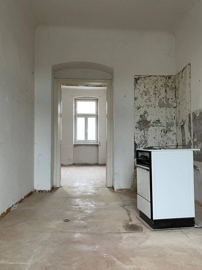 Leere Küche mit altem Herd, Spüle und renovierungsbedürftigen Wänden.