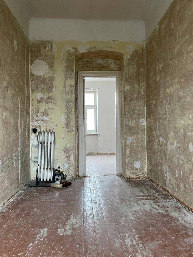 Renovierungsbedürftiger Flur mit abgenutztem Holzboden und freigelegten Wänden.