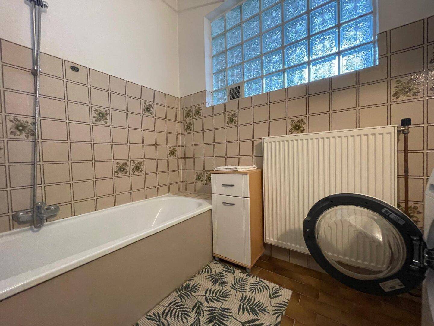 Badezimmer mit Badewanne, Waschbecken, Waschmaschine und Glasbaustein-Fenster.