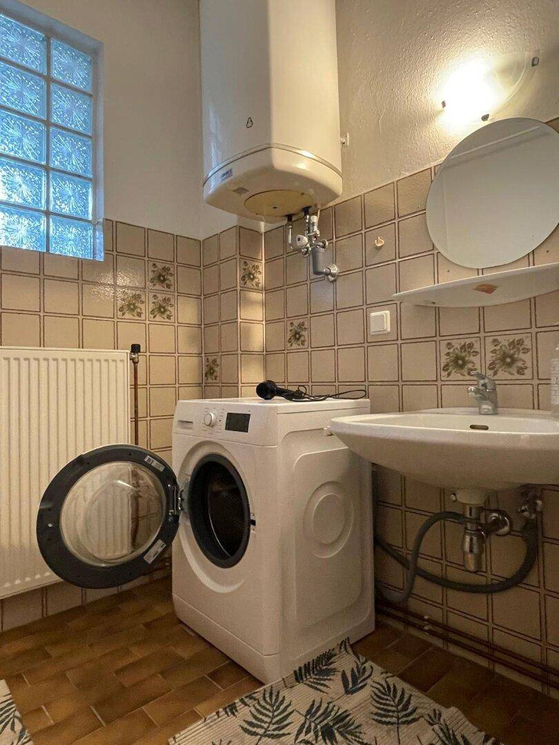 Badezimmer mit Waschbecken, Waschmaschine, Boiler und gemusterten Fliesen.