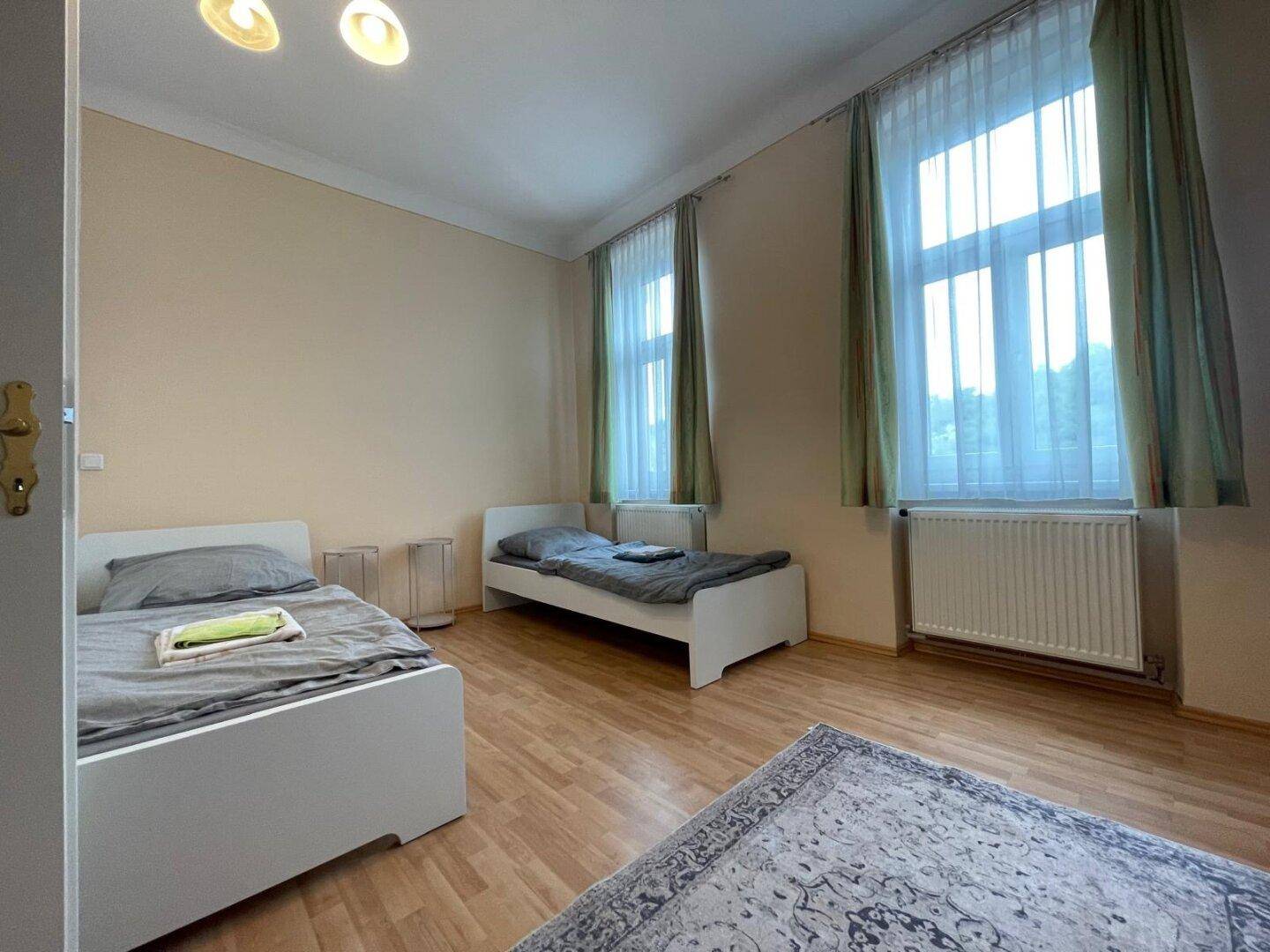 Helles Schlafzimmer mit zwei Betten, Holzboden und grünen Vorhängen.