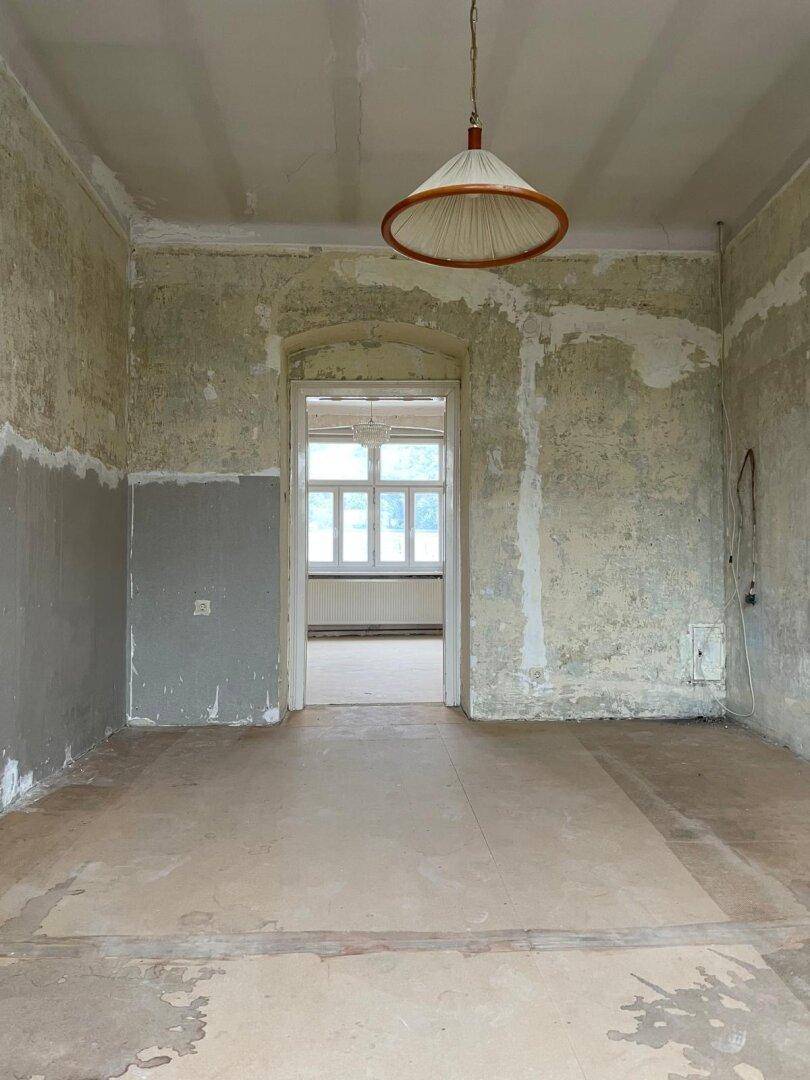 Renovierungsbedürftiges Wohnzimmer mit abgenutzten Wänden und Holzboden.
