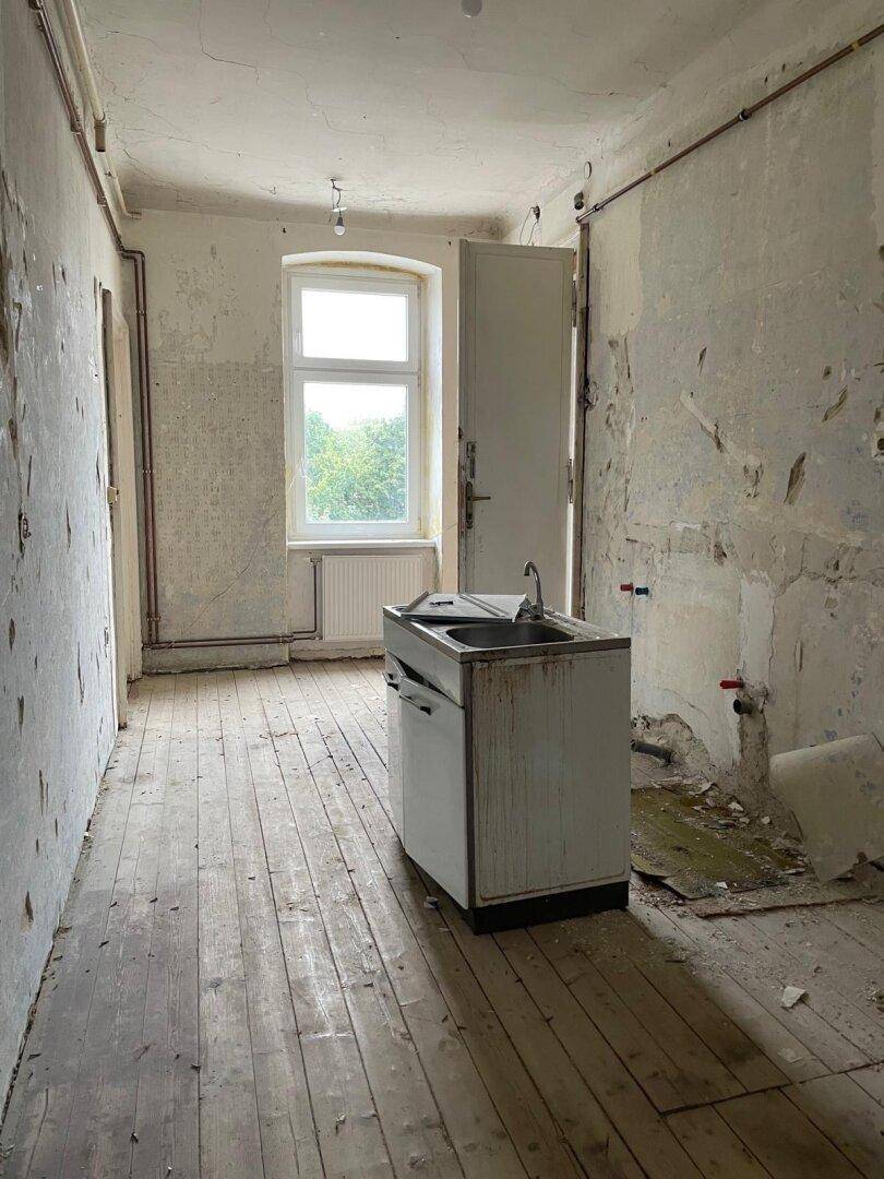 Renovierungsbedürftige Küche mit alter Spüle, Fenster und abgenutztem Holzboden.