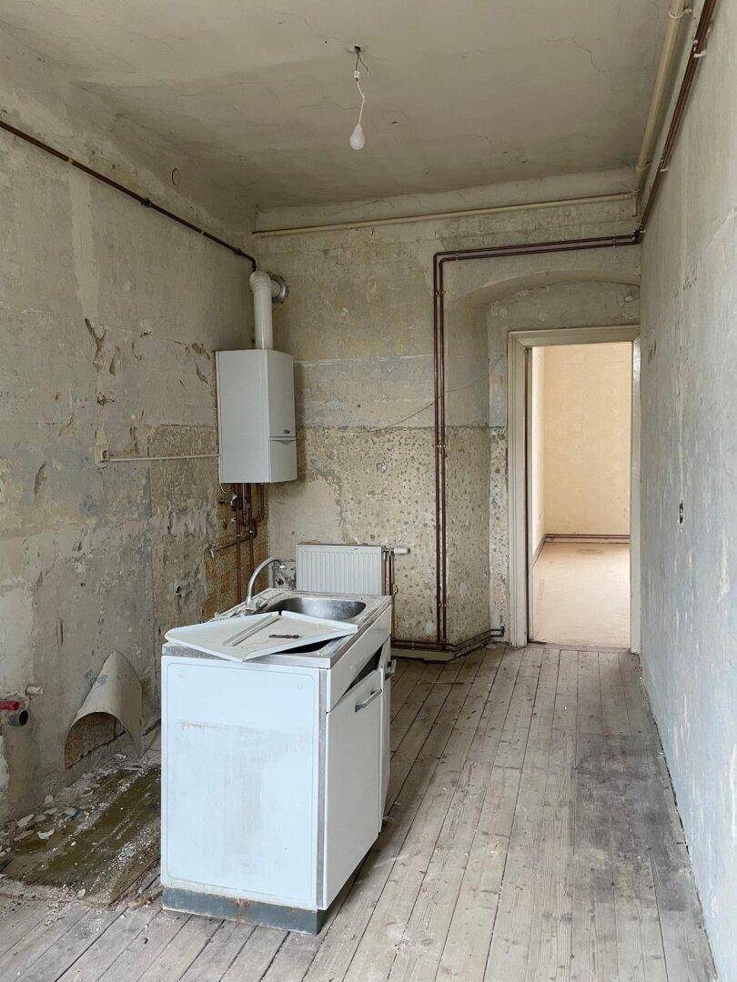 Renovierungsbedürftige Küche mit alter Spüle, Boiler und freiliegenden Rohren.