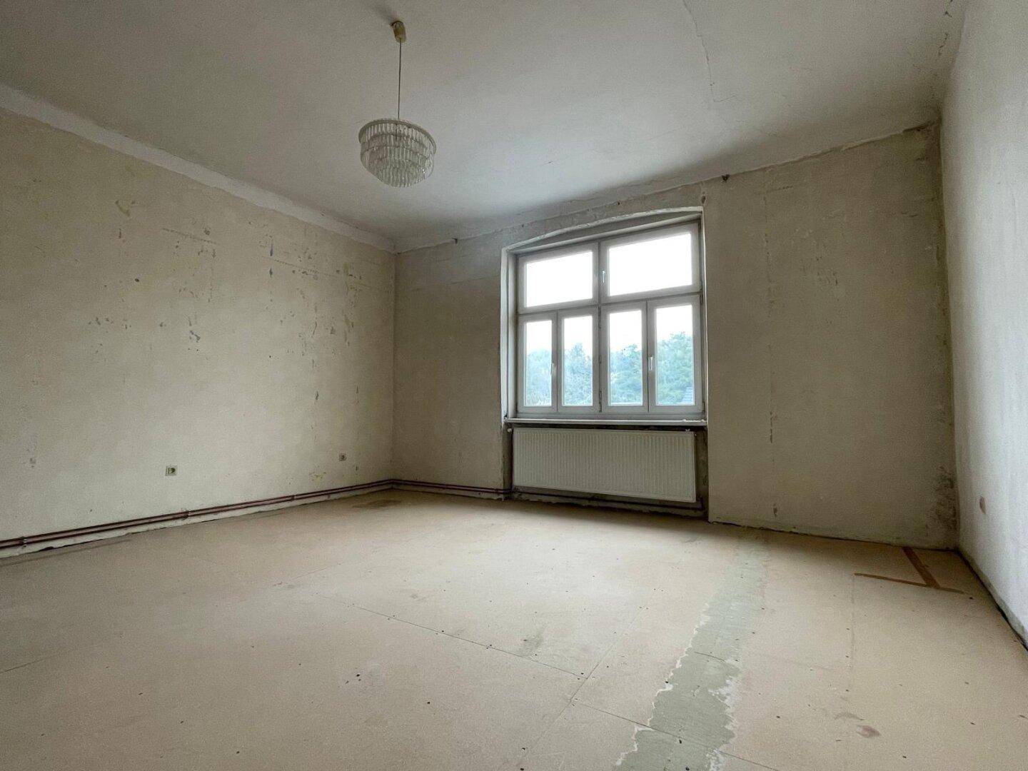 Renovierungsbedürftiges Schlafzimmer mit abgenutztem Boden und großem Fenster.
