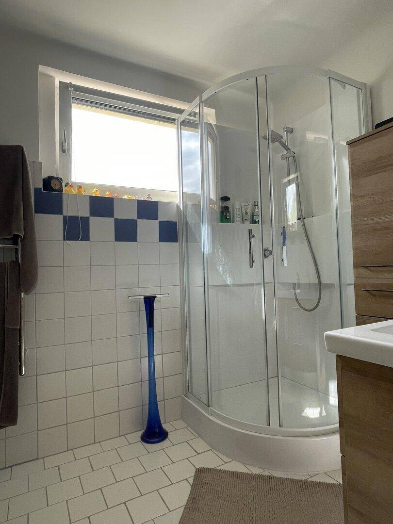 Funktionales Badezimmer mit einer Duschkabine, einem Fenster und weißen Fliesen für eine helle Atmosphäre.