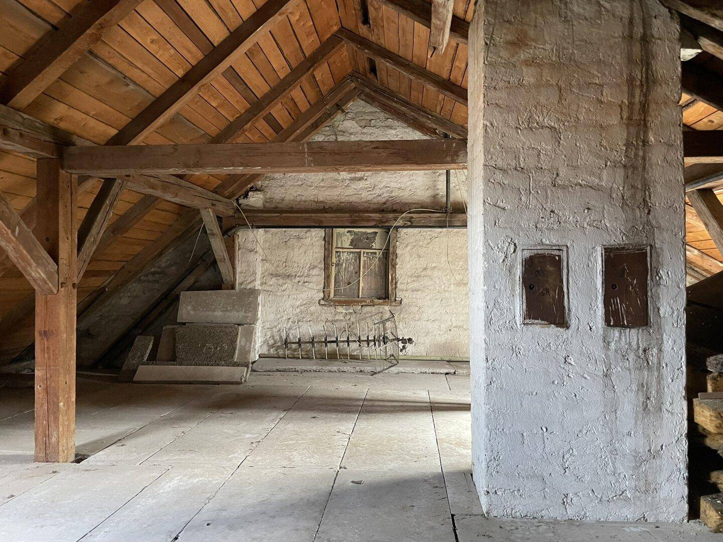 Unausgebauter Dachboden mit sichtbaren Holzbalken und rustikalen Wänden, bietet Ausbaupotenzial.