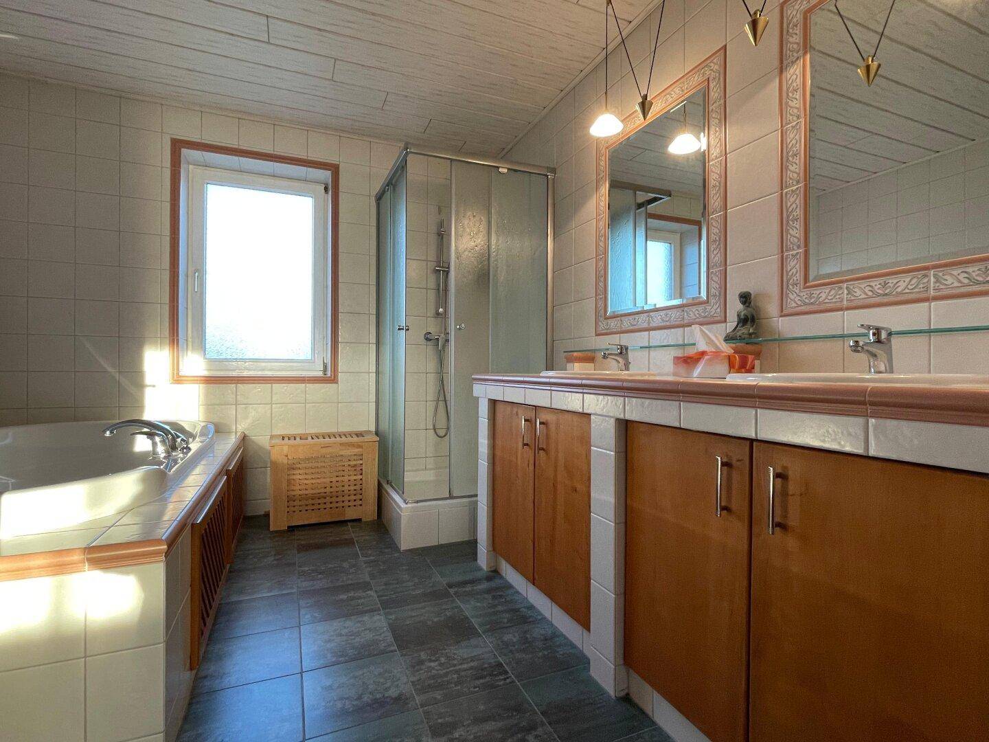 Badezimmer mit Doppelwaschbecken, Dusche und Badewanne, hell durch das Fenster.