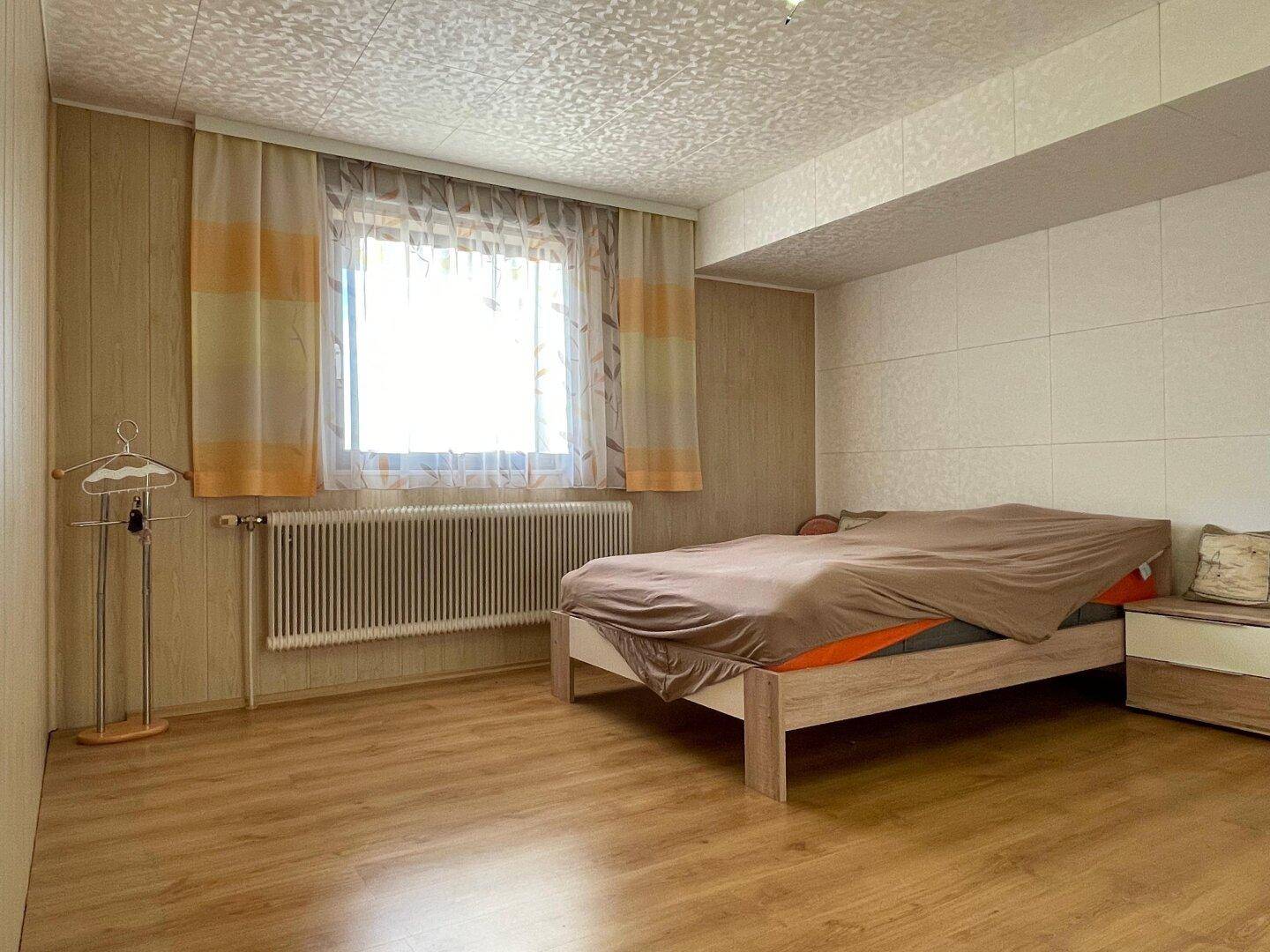 Schlafzimmer mit Laminatboden, großem Fenster und Heizkörper unter der Fensterbank.