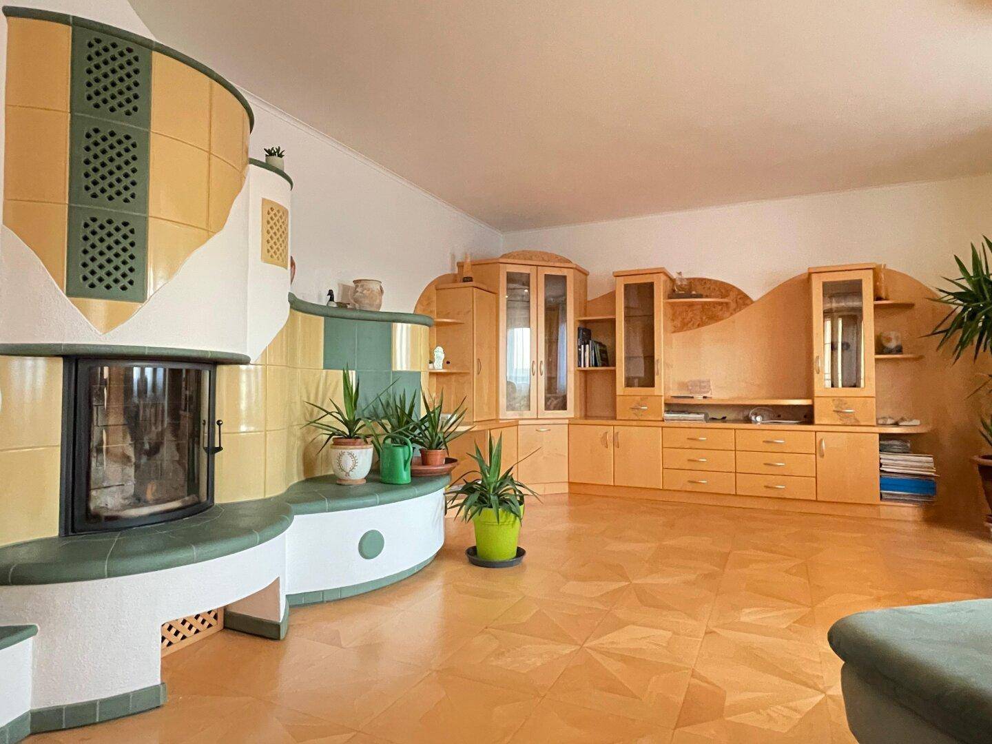 Geräumiges Wohnzimmer mit einem großen, farbenfrohen Kachelofen und Holzparkettboden.