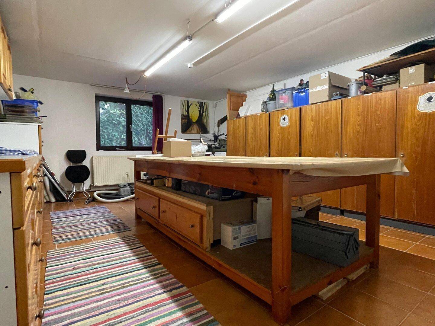 Geräumiger Hobbyraum im Untergeschoss mit großem Arbeitstisch und vielen Schränken.