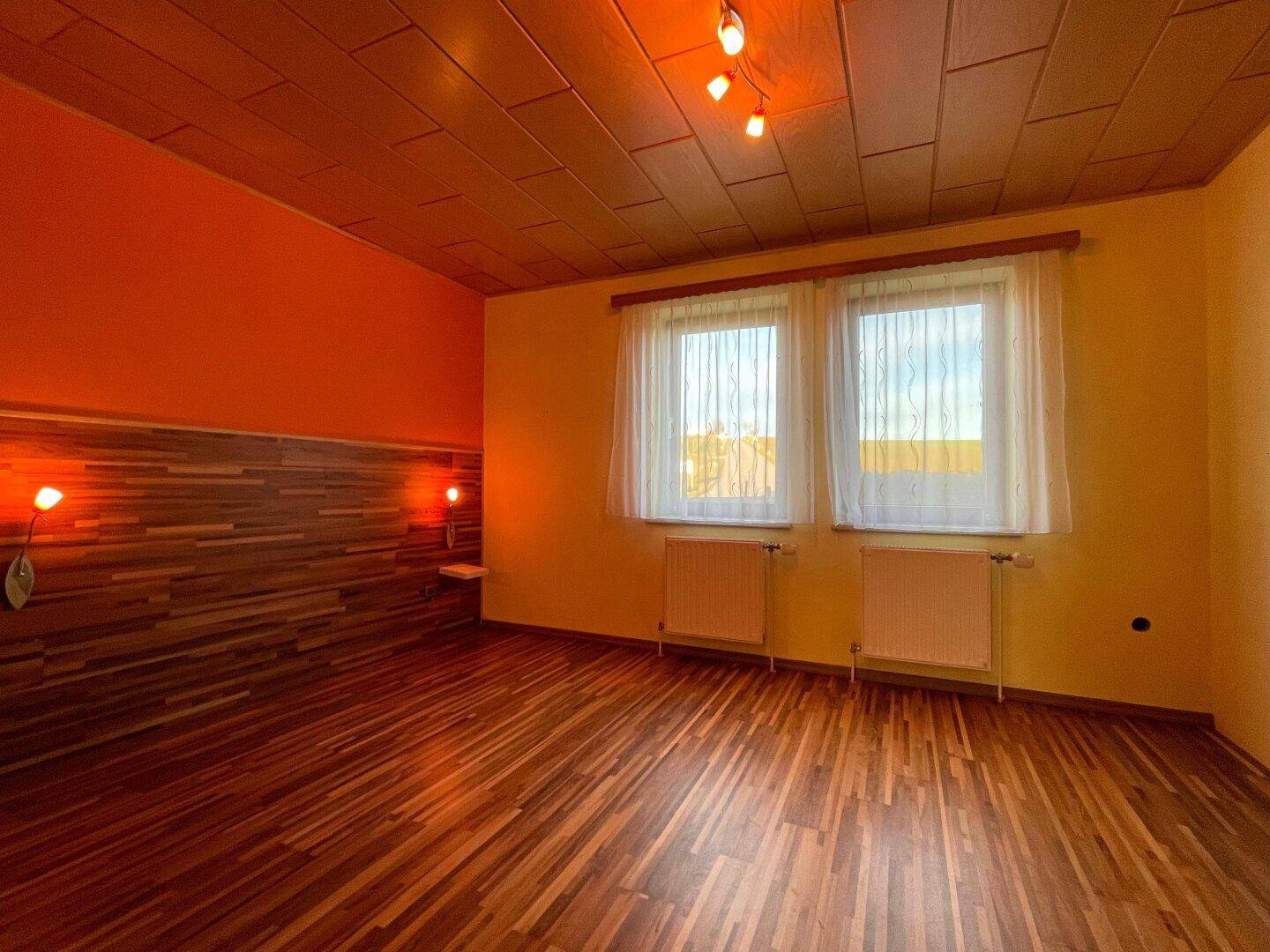 Schlafzimmer mit auffälligen orangefarbenen Wänden, Holzdecke und Laminatboden.