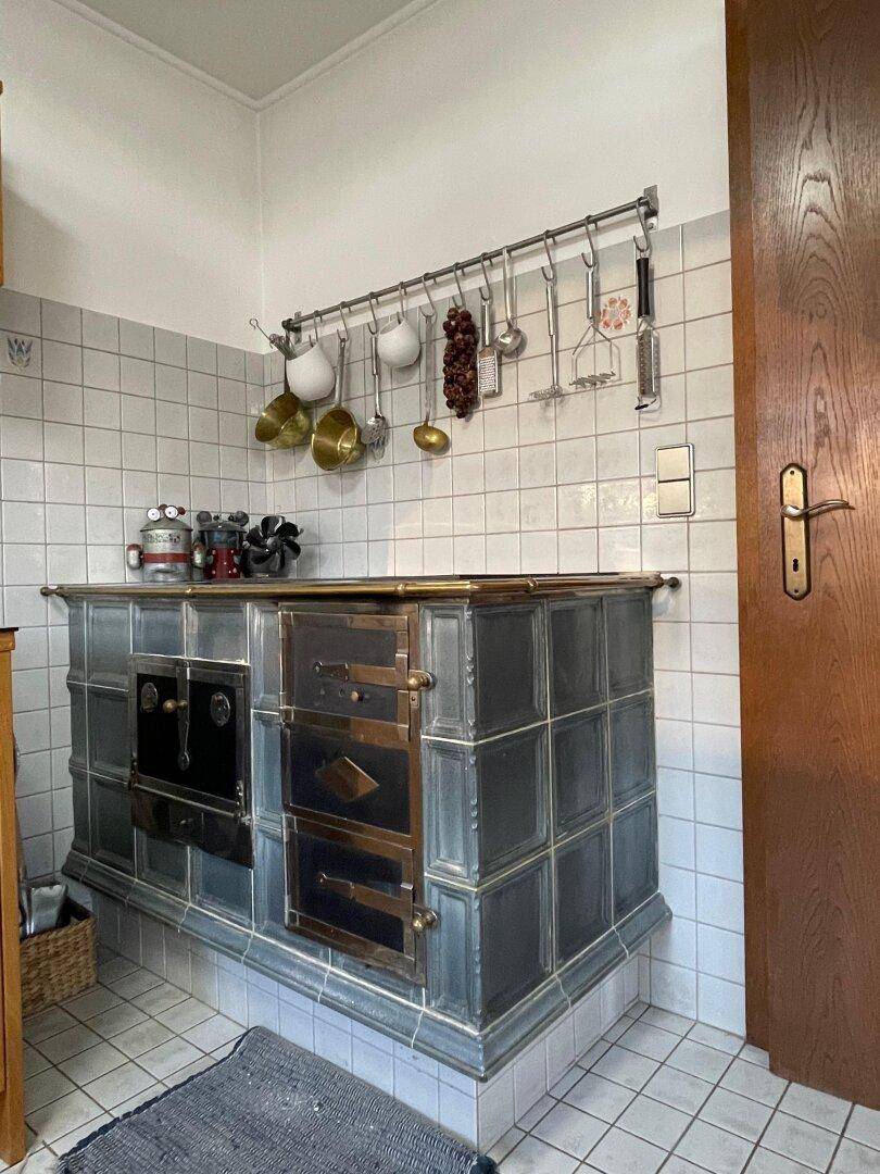 Traditioneller Kachelofen in der Küche, umgeben von weißen Fliesen und Kochutensilien.