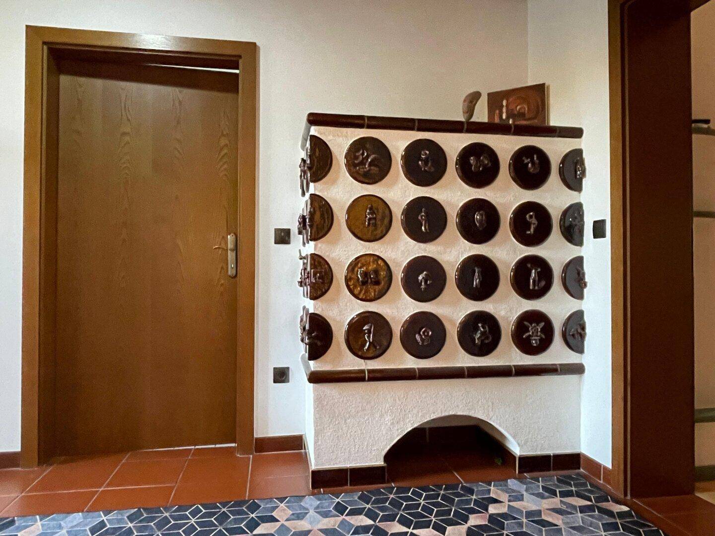 Flur mit einem verzierten Kachelofen und Terrakotta-Fliesenboden.