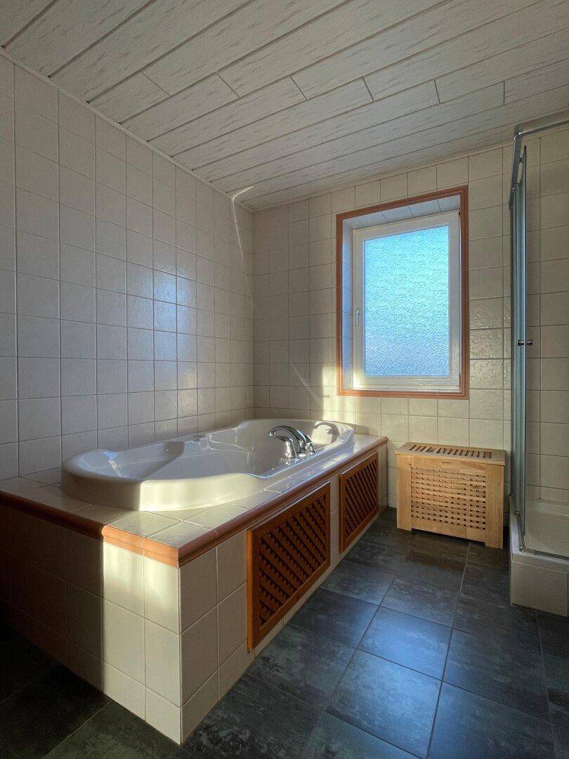 Badezimmer mit eingebauter Badewanne, Dusche und Fenster für natürliche Belüftung.