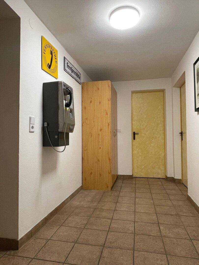Schlichter Flur im Untergeschoss mit Fliesenboden und einem Wandtelefon im Retro-Stil.