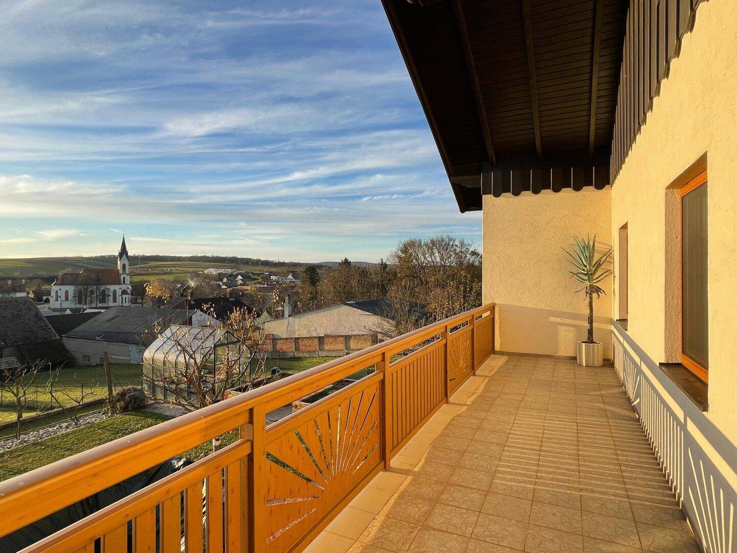 Langer Balkon mit Holzgeländer und weitem Blick über die ländliche Umgebung und ein Dorf.