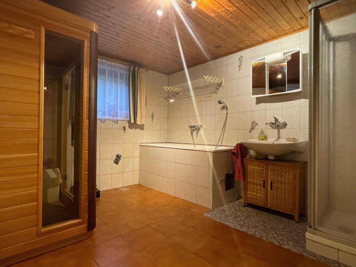 Badezimmer im Untergeschoss mit Sauna, Badewanne, Dusche und Holzdecke.