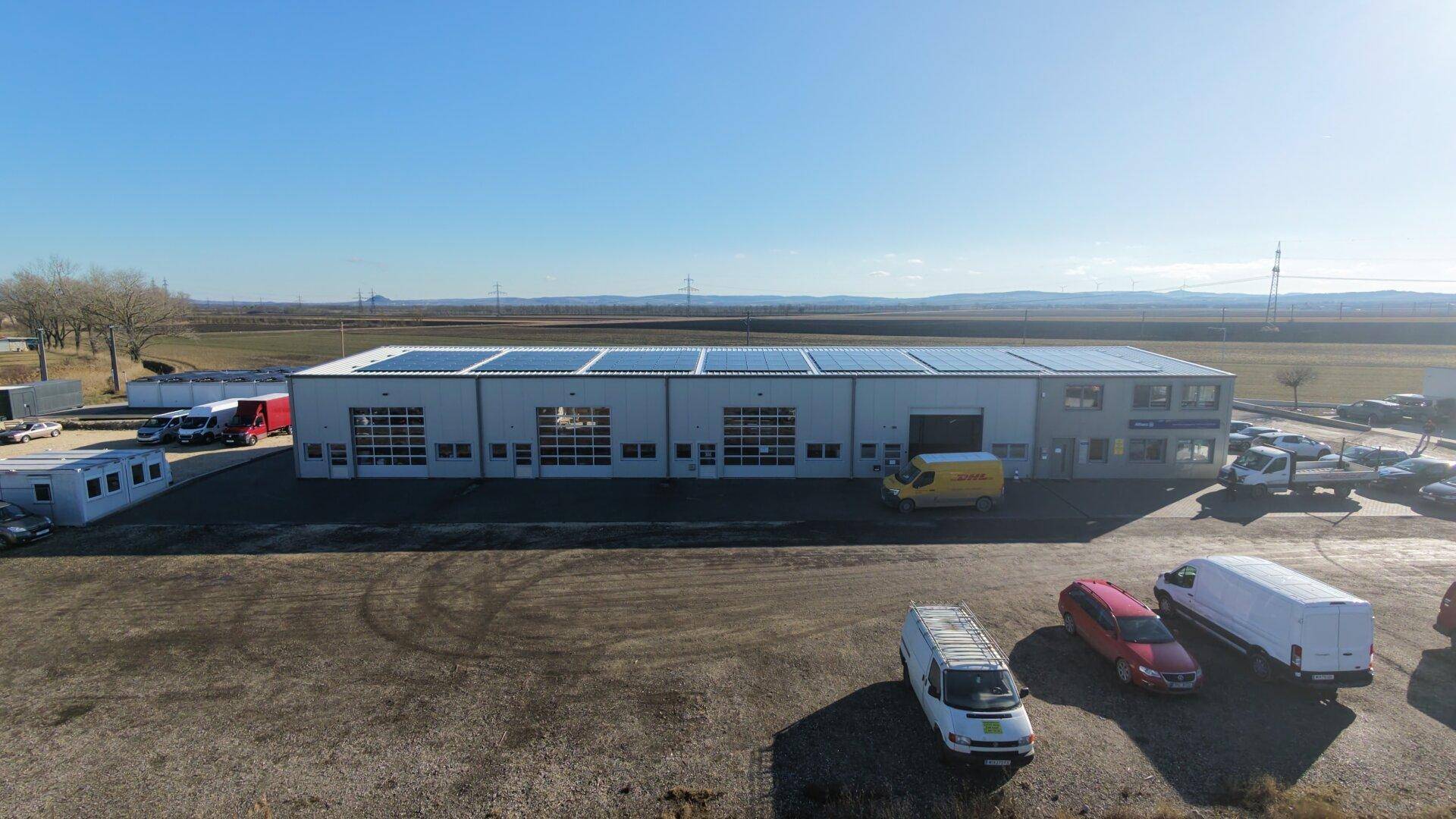 Ansicht des modernen Gewerbegebäudes mit Photovoltaikanlage auf dem Dach und mehreren Garagentoren.