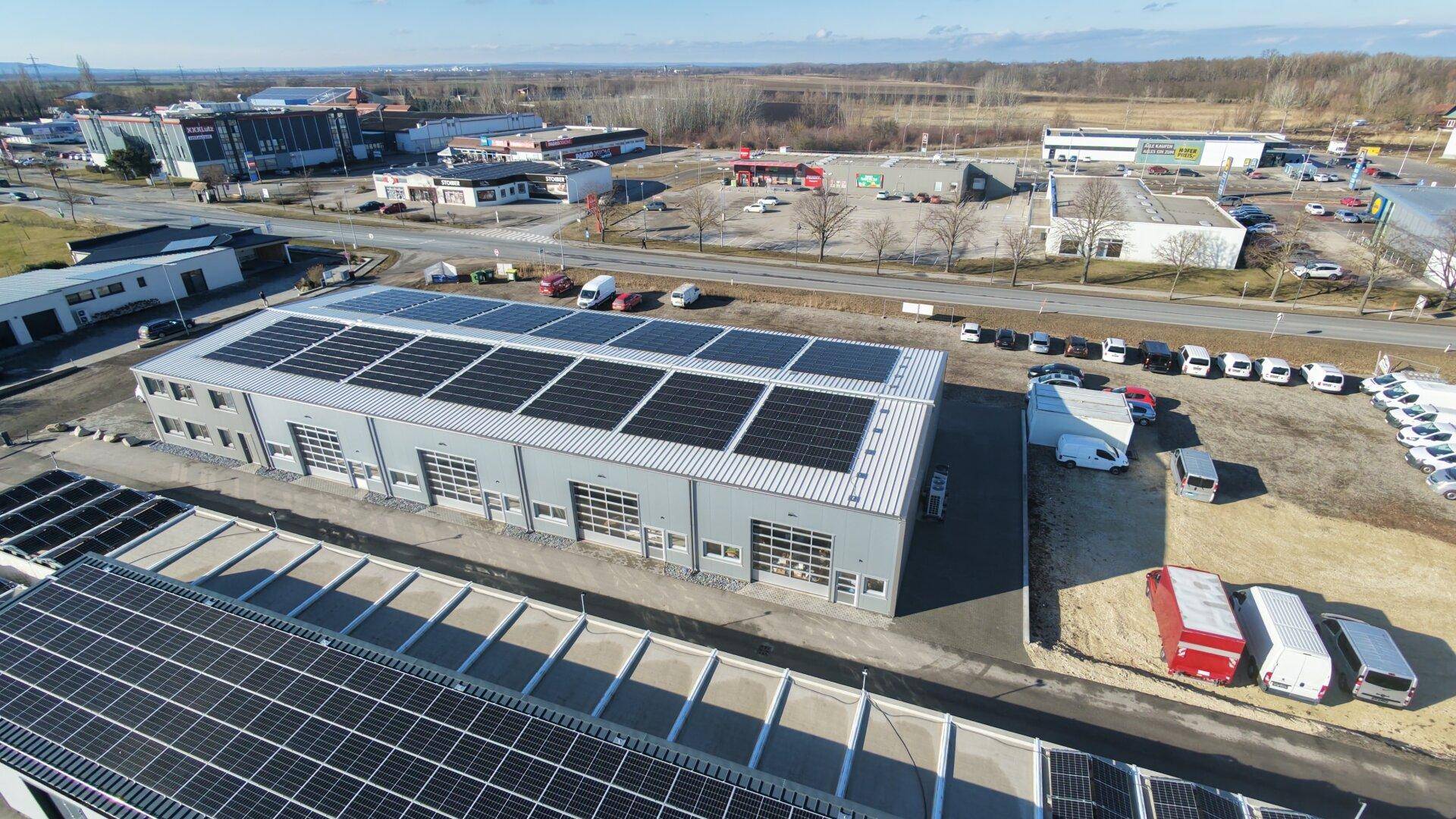 Luftaufnahme des Gewerbegebäudes mit umfassender Photovoltaikanlage auf dem Dach und angrenzenden Parkflächen.