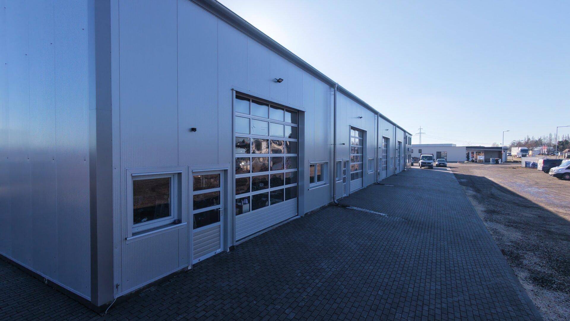 Seitenansicht des Gewerbegebäudes mit mehreren großen Garagentoren und gepflastertem Zufahrtsbereich.