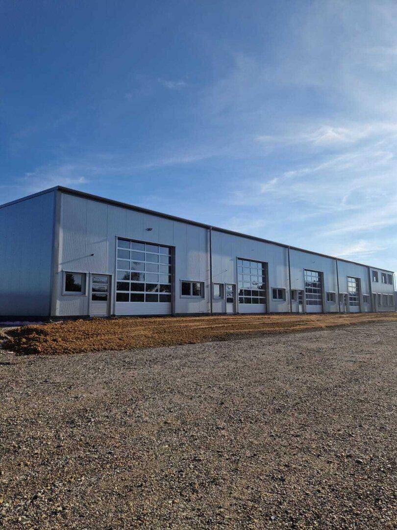 Weitwinkelansicht der modernen Gewerbehalle mit mehreren Garagentoren und einem weiten Vorplatz unter blauem Himmel.