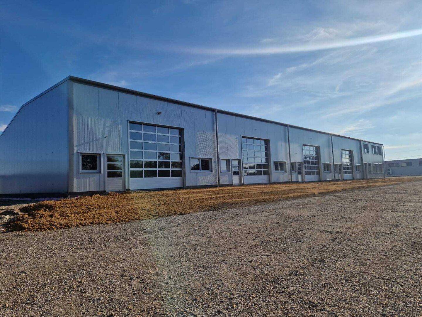 Ansicht der modernen Gewerbehalle mit großen Garagentoren und einem weiten Vorplatz unter klarem Himmel.