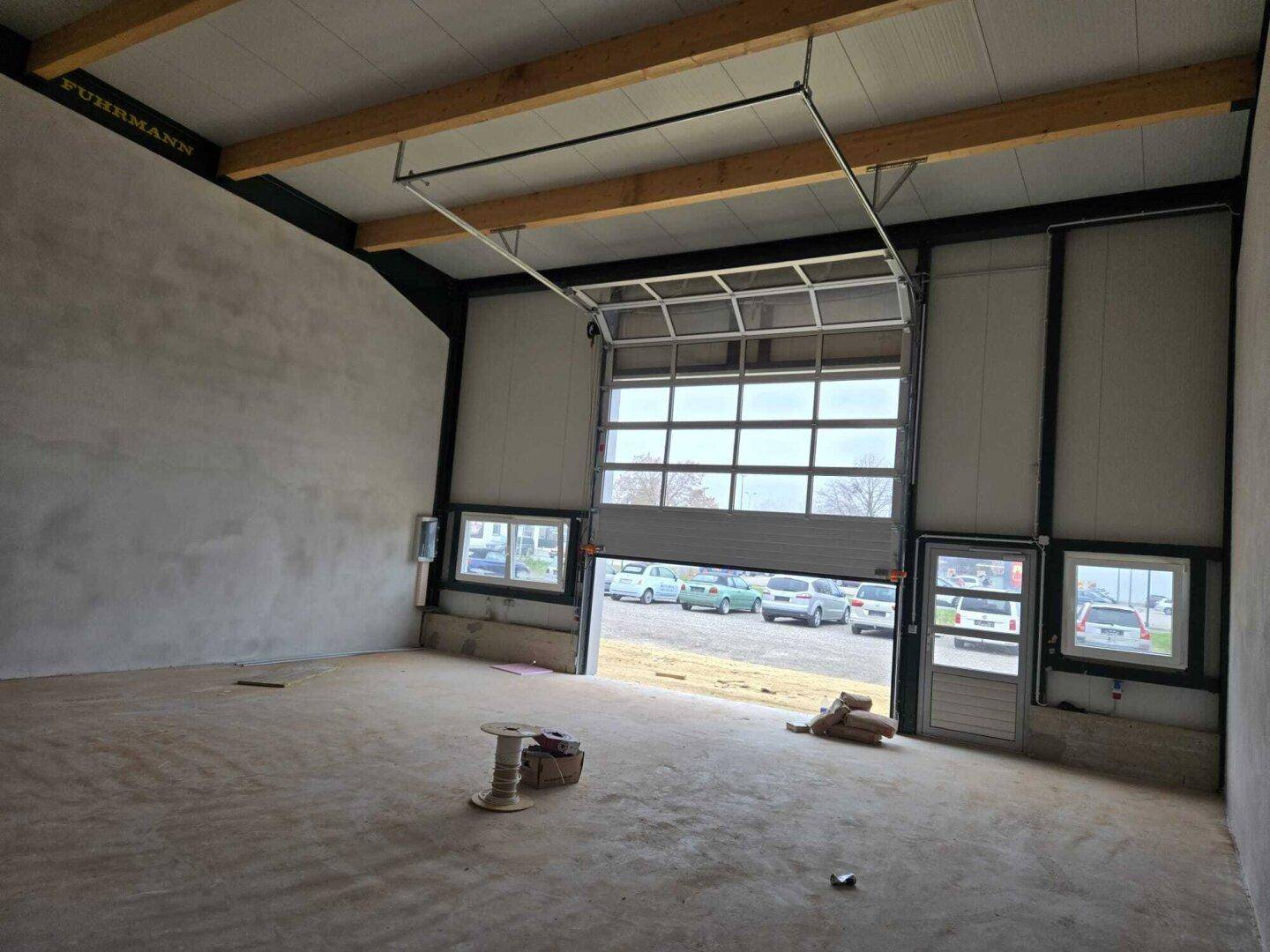 Innenansicht einer Lagerhalle mit geöffnetem Sektionaltor, das Tageslicht hereinlässt und Blick nach draußen bietet.