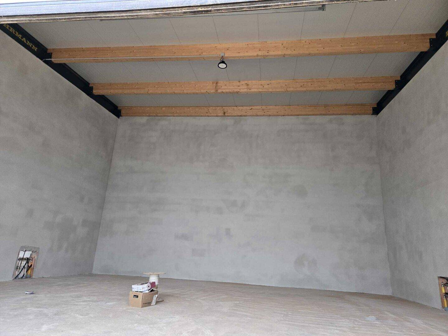 Geräumige Lagerhalle mit hohen Decken, sichtbaren Holzbalken und einer großen, leeren Betonwand.