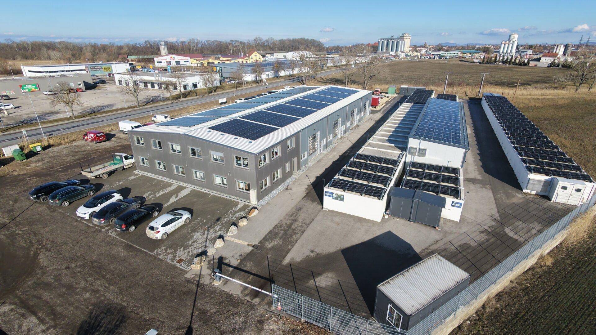 Gesamtansicht des Gewerbekomplexes mit Hauptgebäude, Containern und Solaranlagen in ländlicher Umgebung.