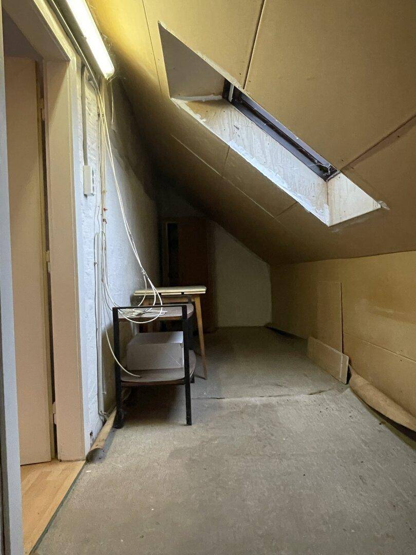Unausgebauter Dachbodenbereich mit Schrägen, Dachfenster und einfacher Beleuchtung.