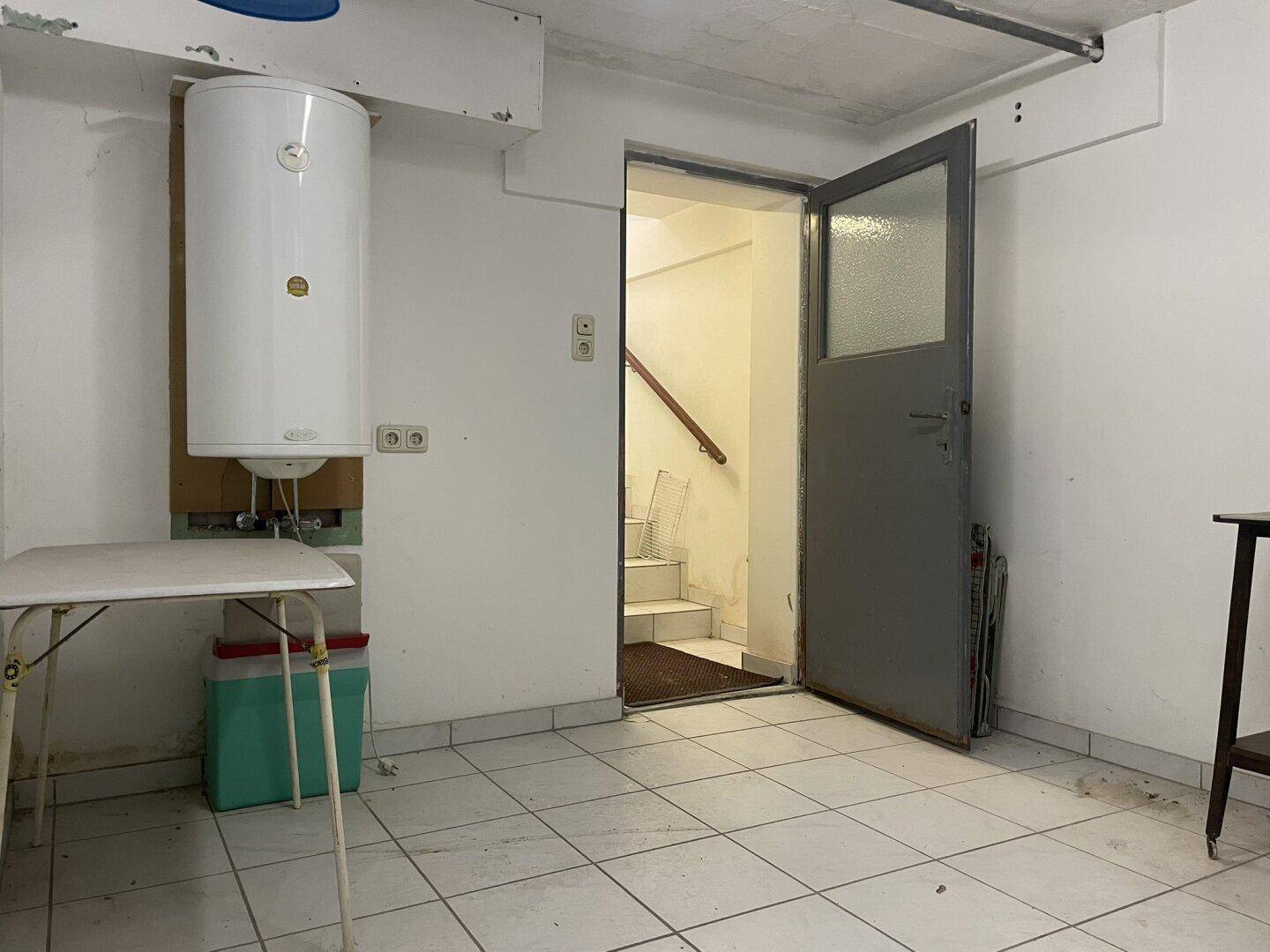 Kellerraum mit Warmwasserboiler, gefliestem Boden und Zugang zu einer Treppe.