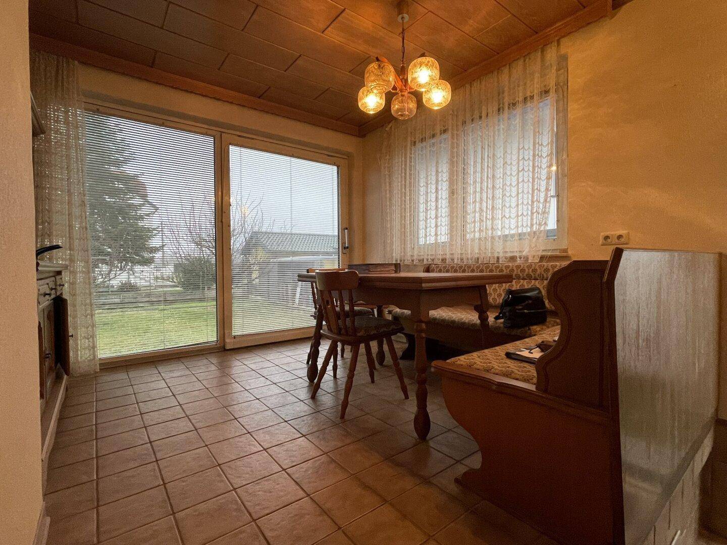 Gemütlicher Essbereich mit Holztisch, gefliestem Boden und Blick in den Garten.