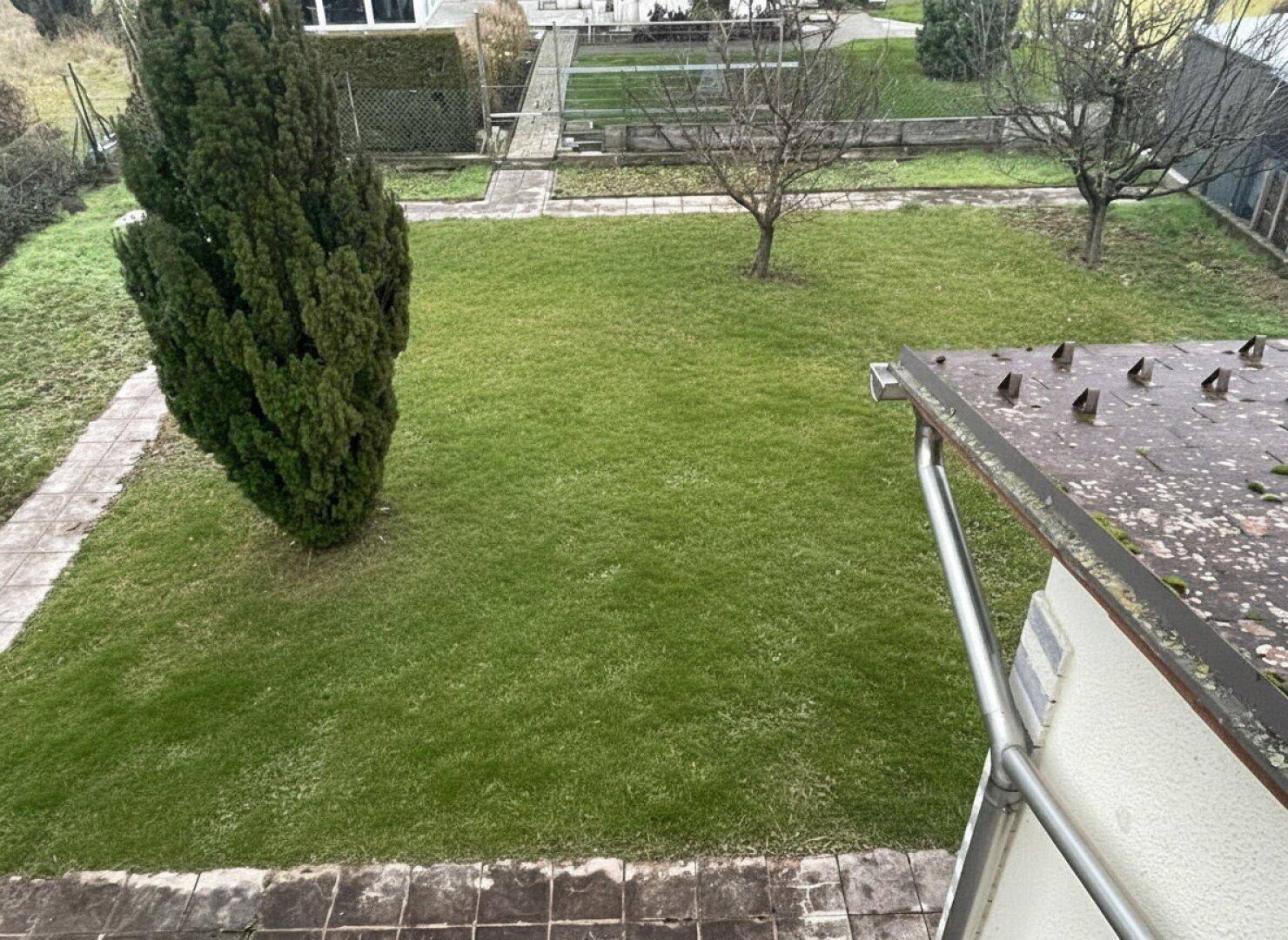 Blick von oben auf den gepflegten Garten mit Rasenfläche und Bäumen.