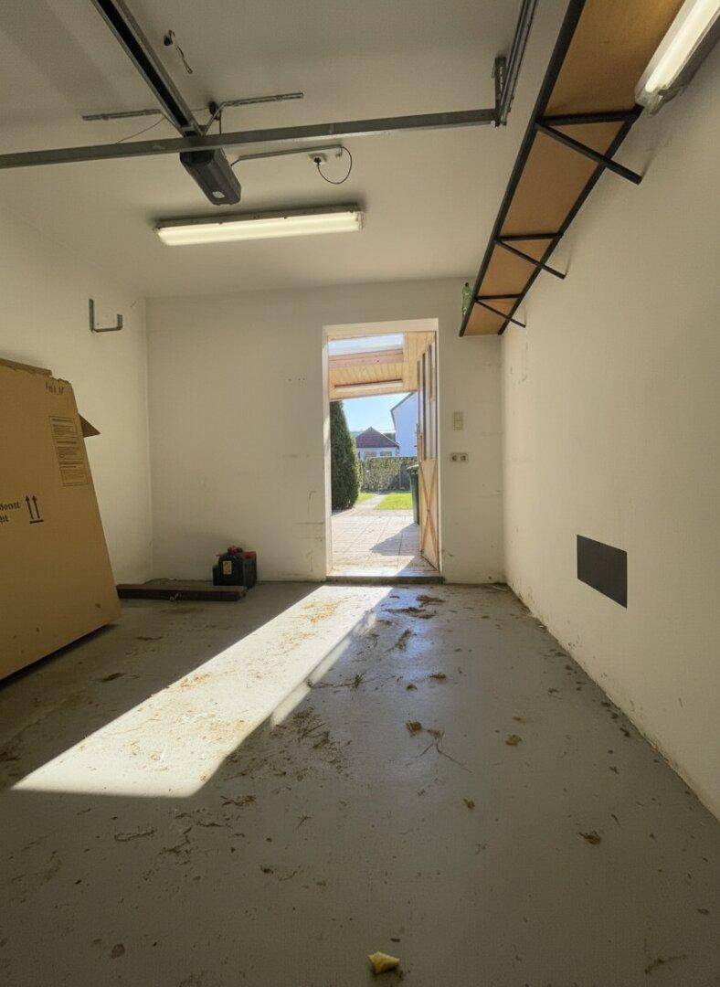 Garage mit Betonboden und Ausgang zum Garten, hell durch Tageslicht.
