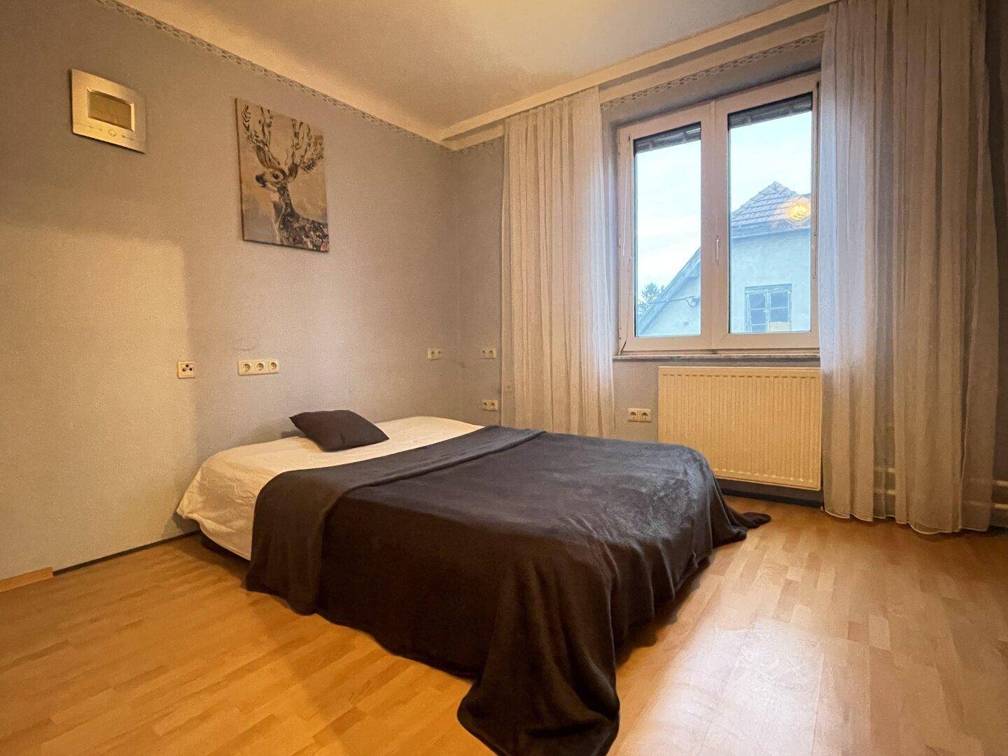 Helles Schlafzimmer mit Parkettboden, Doppelbett und Fenster mit Blick auf die Umgebung.